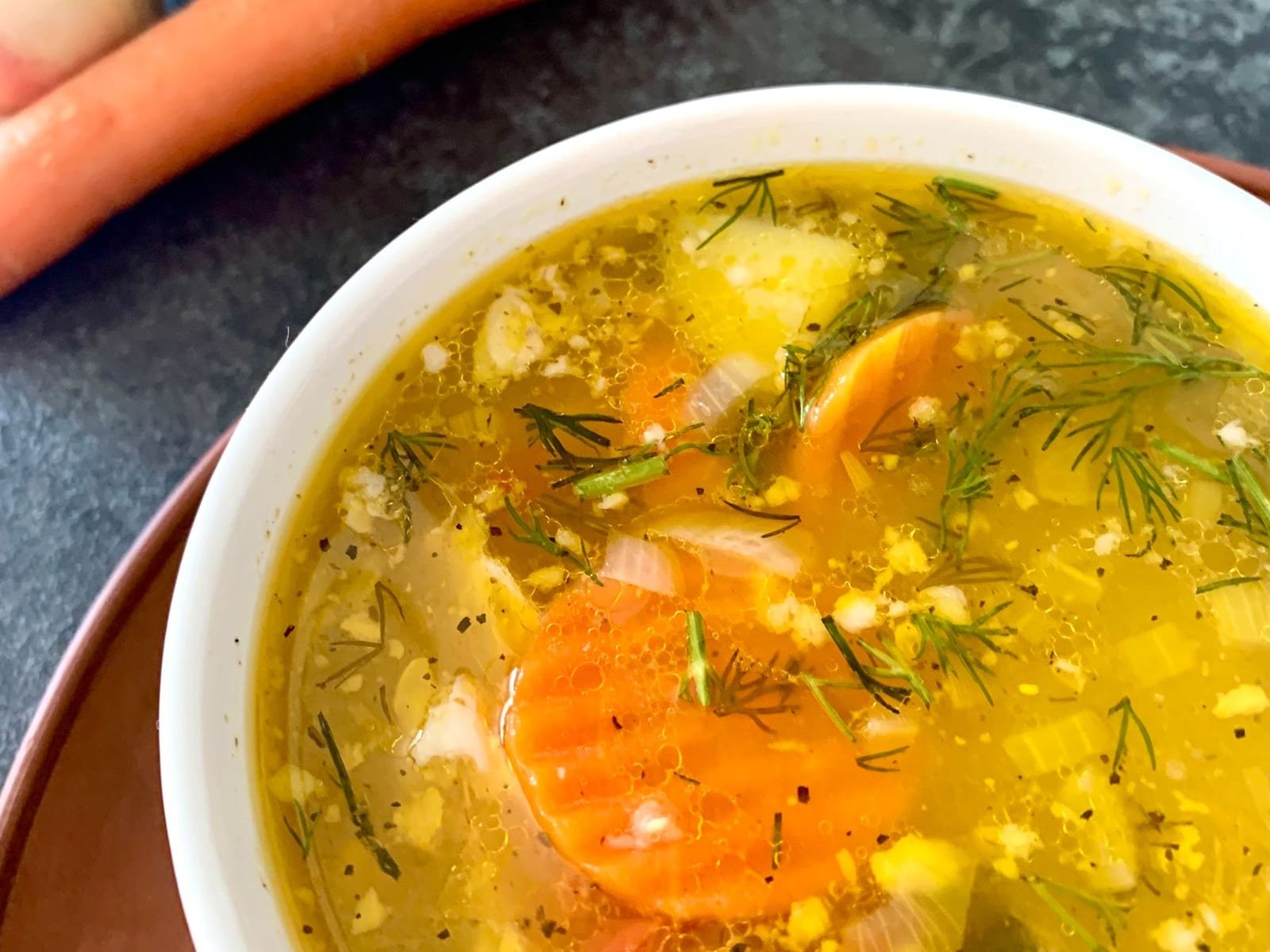 A bowl of golden vegetable soup with carrots and herbs