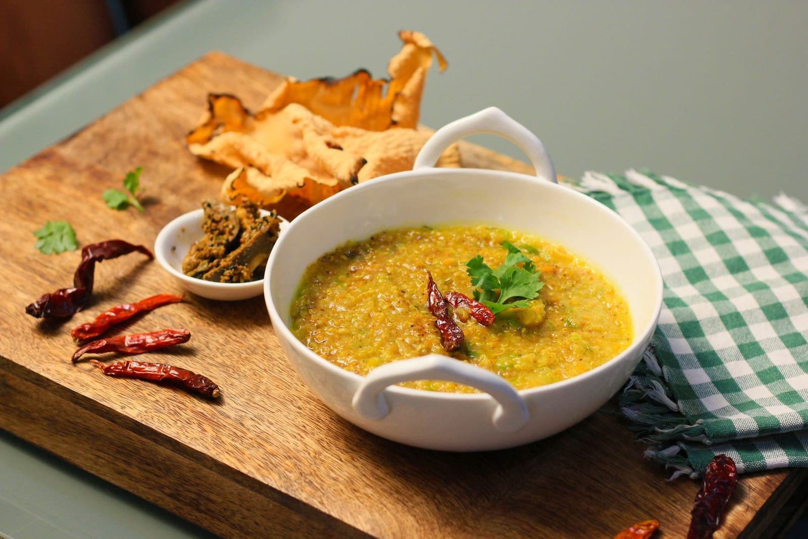 A bowl of vegetable khichdi garnished with coriander and dried red chillies, served with papad and pickle